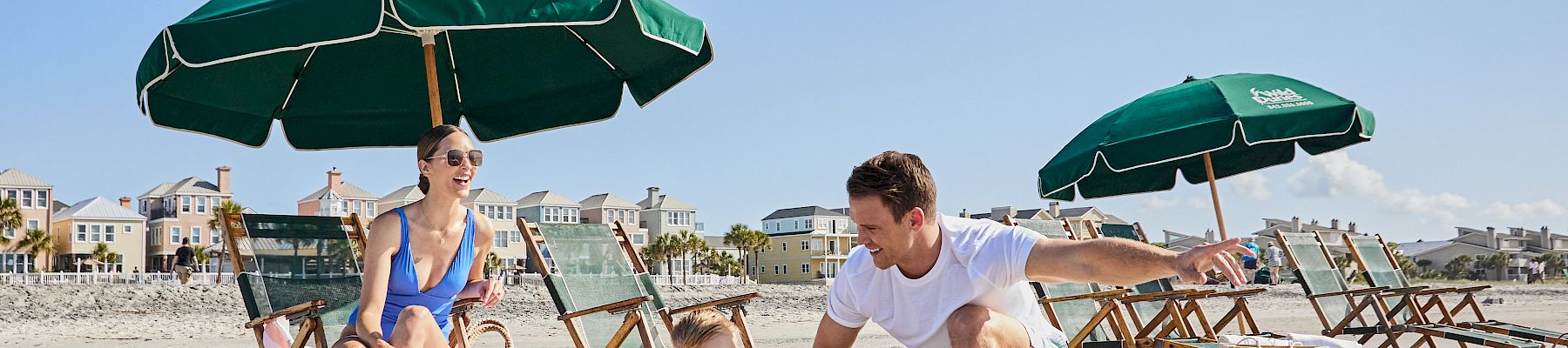 A family enjoys a sunny day at the beach, with umbrellas and chairs set up, as the child plays in the sand.