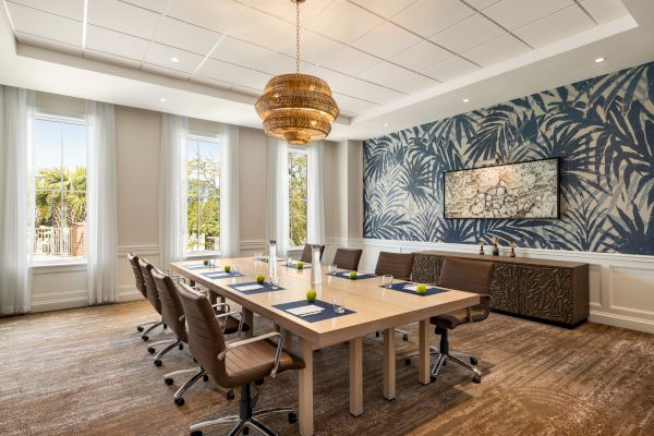 A modern conference room with a wooden table, chairs, and decorative wall art, featuring natural light from large windows.