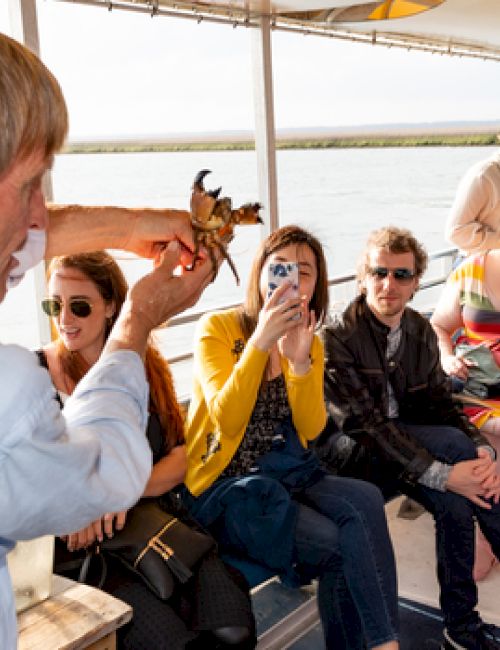 A person is showing something to a group on a boat. The onlookers are taking photos, capturing the presentation attentively.